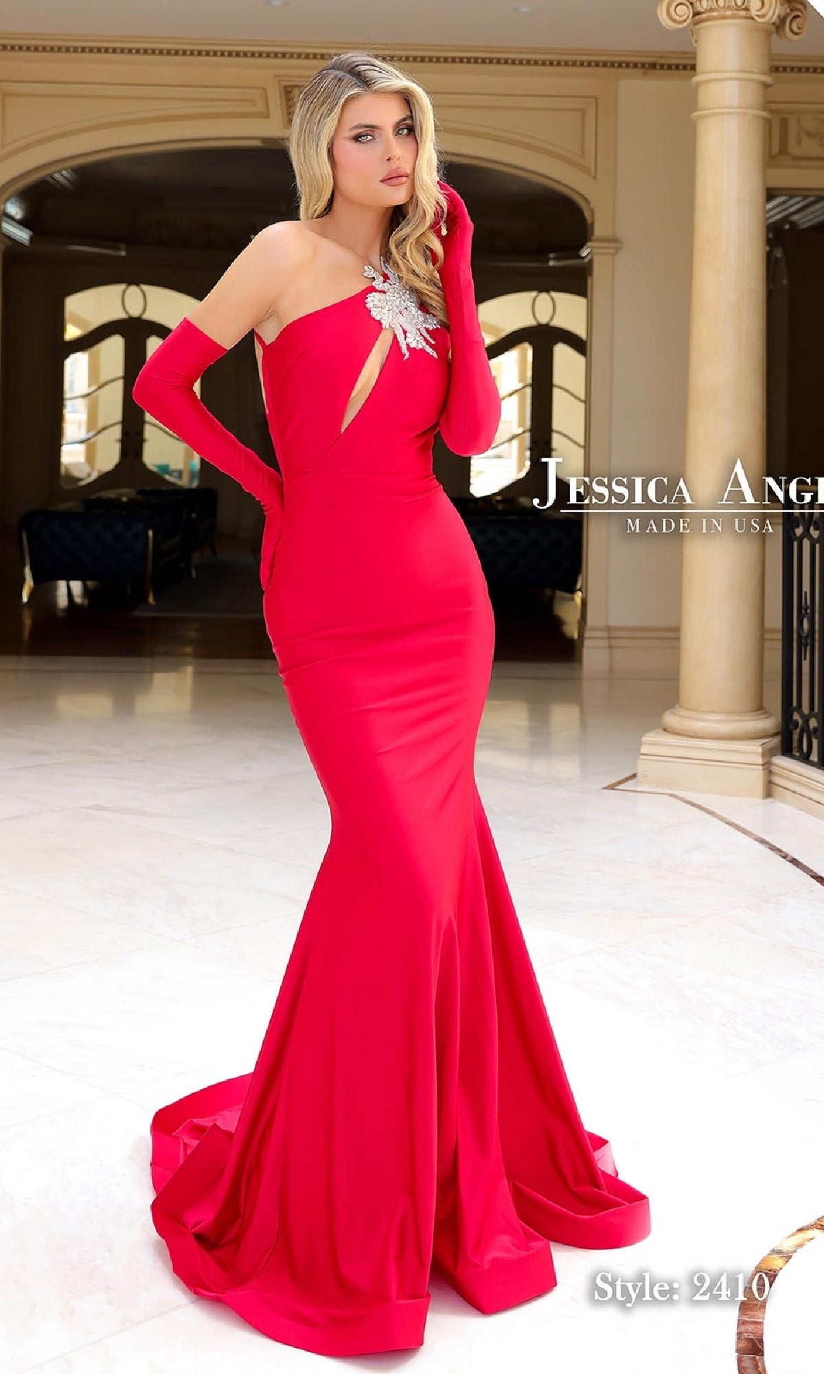A woman indoors wears the Jessica Angel 2410 Long Cut-Out Prom Dress—a fitted, floor-length red gown with a keyhole cutout, silver embellishment, and matching red gloves.